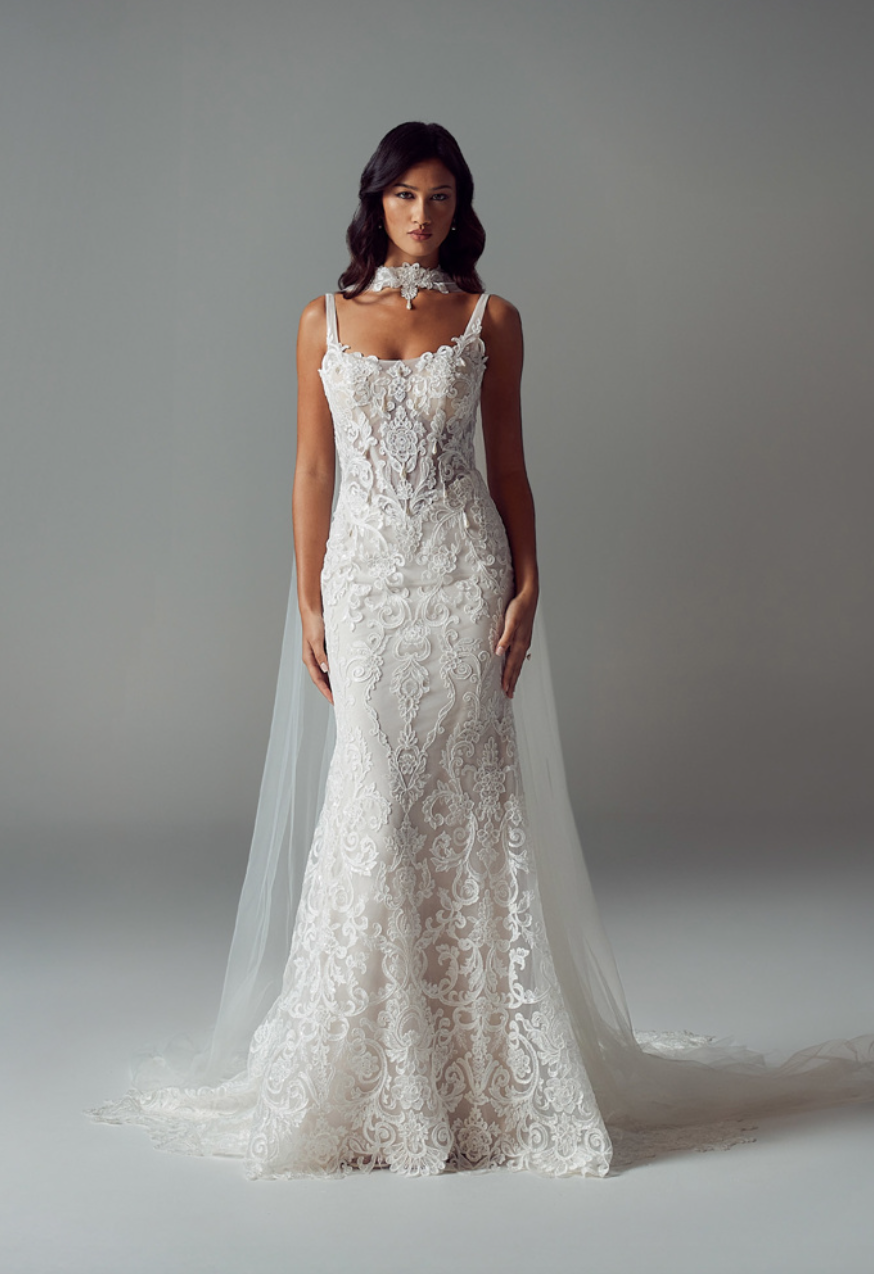 A model wears a white, floor-length, lace mermaid-style wedding gown with thin straps and a matching sheer choker.