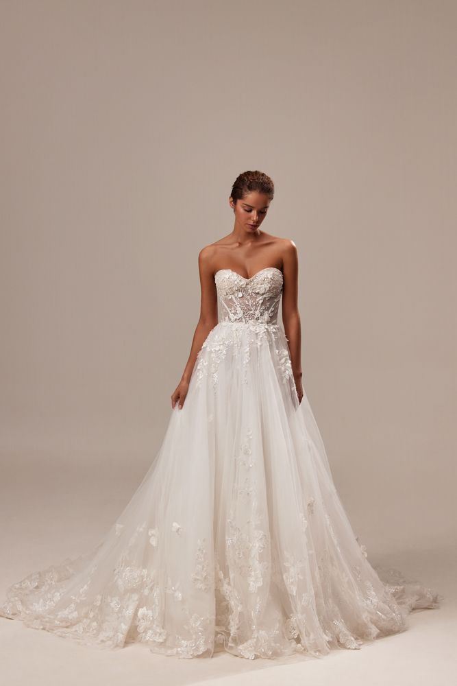 A model wearing a strapless, floral-appliqué A-line wedding dress with a long train against a plain light background.
