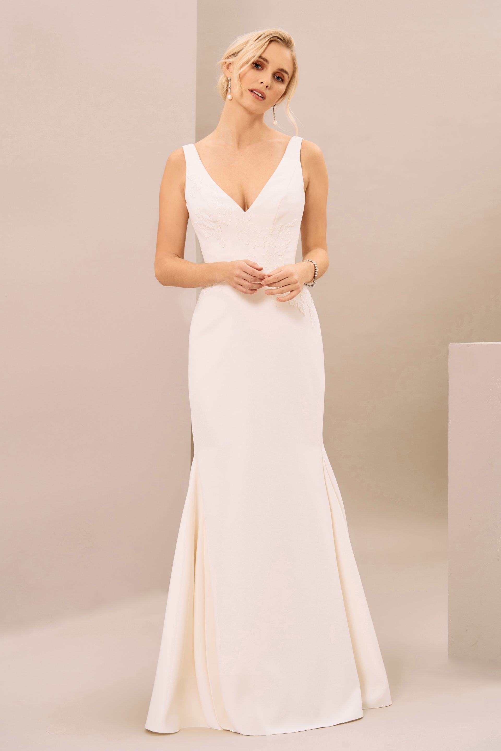 A person wearing a sleeveless, ivory, V-neck, floor-length bridal gown with a fitted bodice and flared skirt.