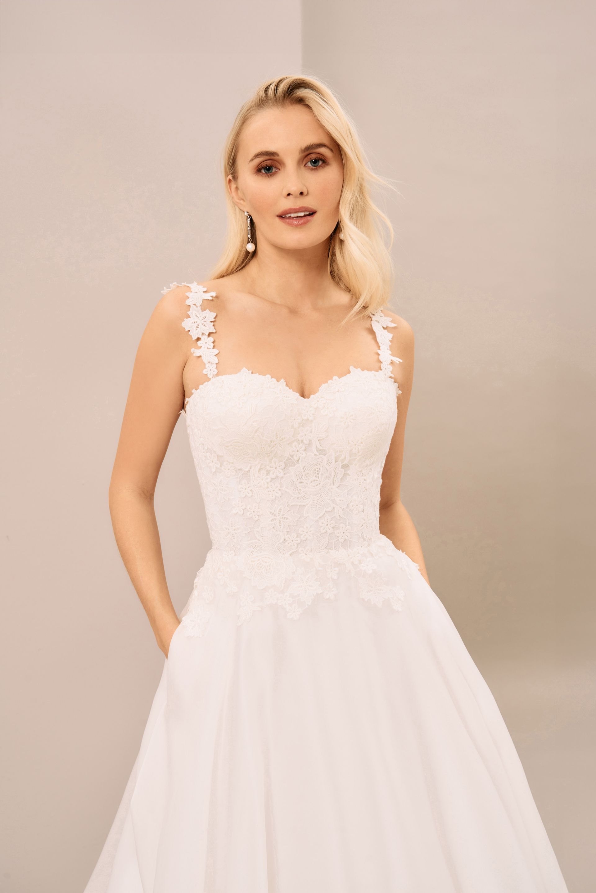 A person wearing a white, floor-length wedding dress with a lace bodice, sweetheart neckline, and delicate straps.