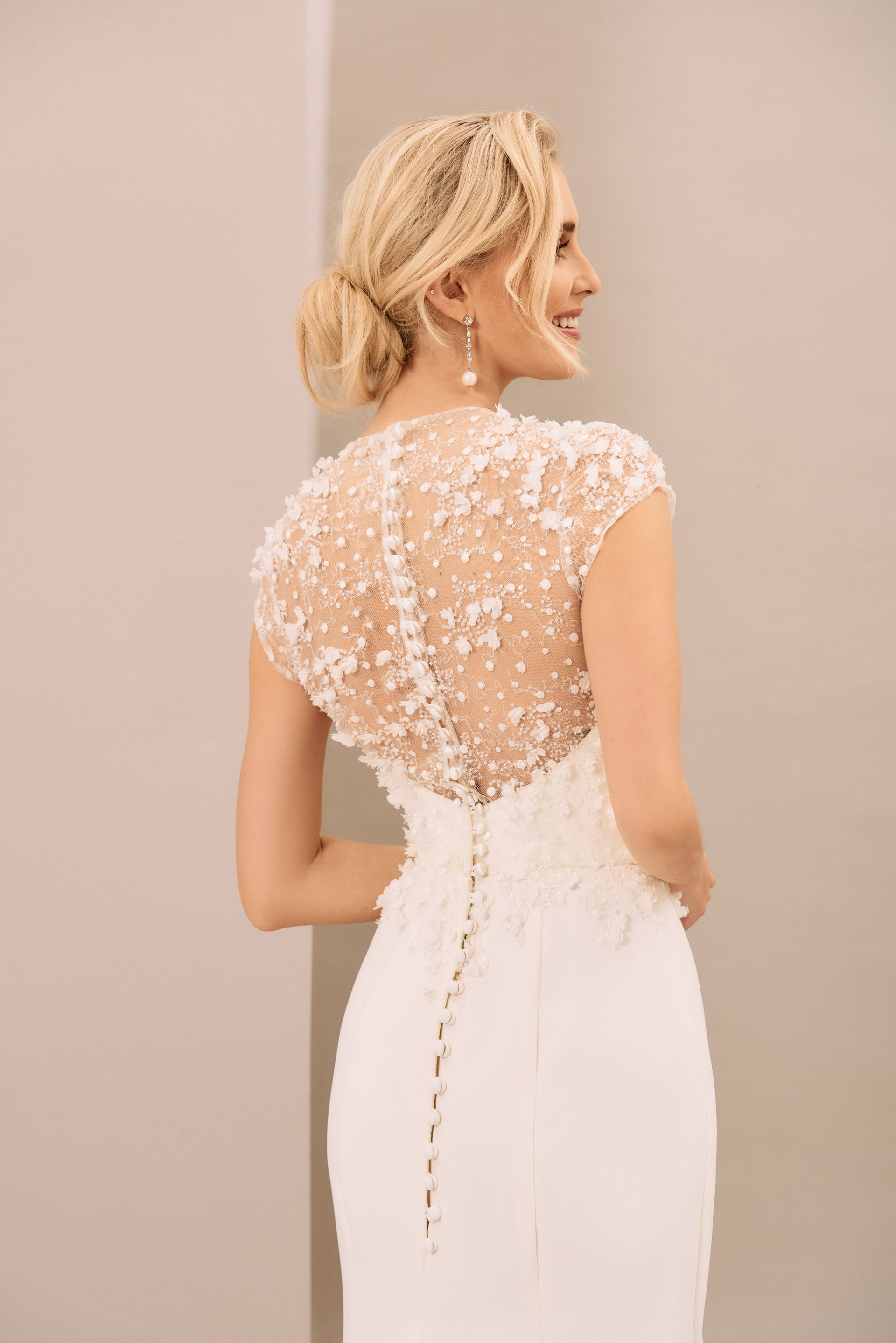 A person in a white wedding gown with a beaded, illusion-neckline back and a vertical row of delicate buttons.