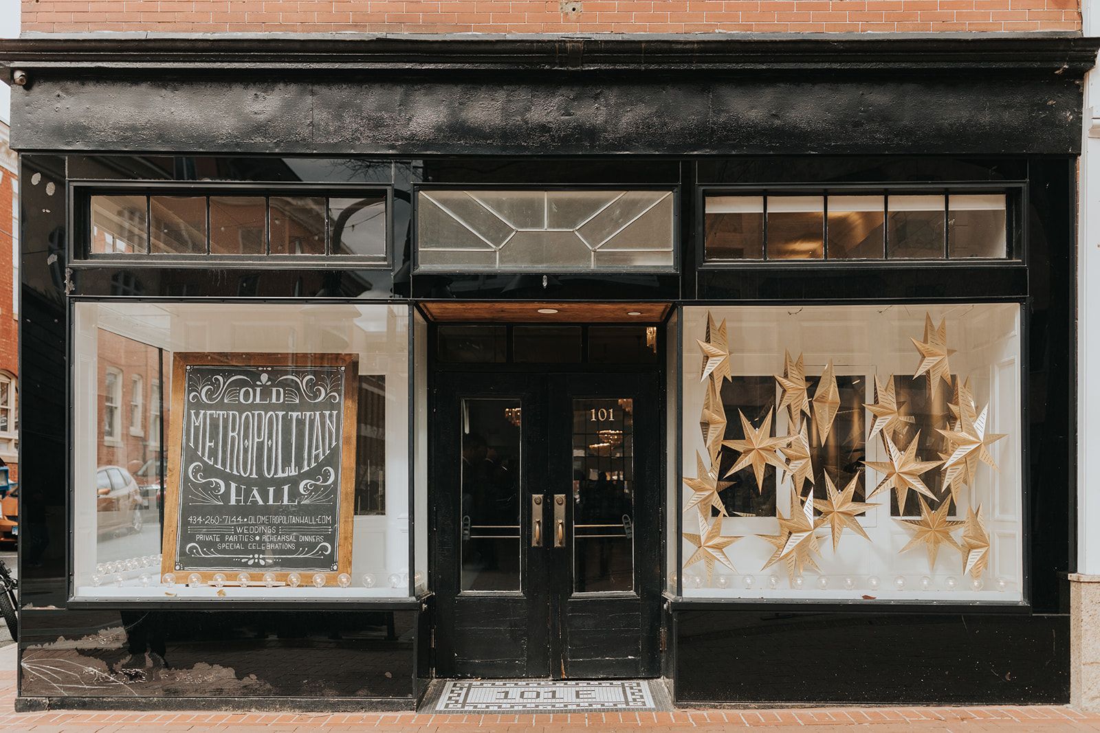 A black storefront with a chalkboard sign in one window and gold star decorations hanging in the other.