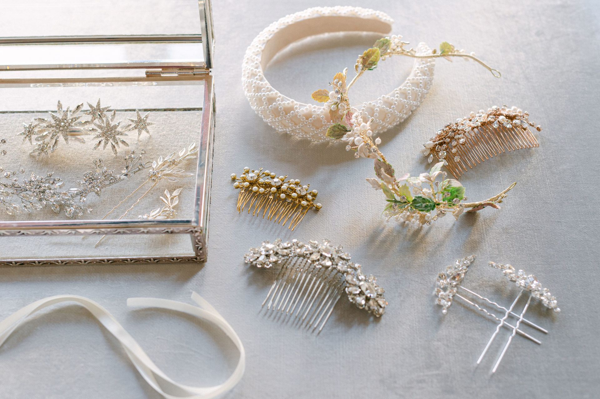 An assortment of bridal hair accessories, including a pearl headband, hair combs, pins, and a glass jewelry box.