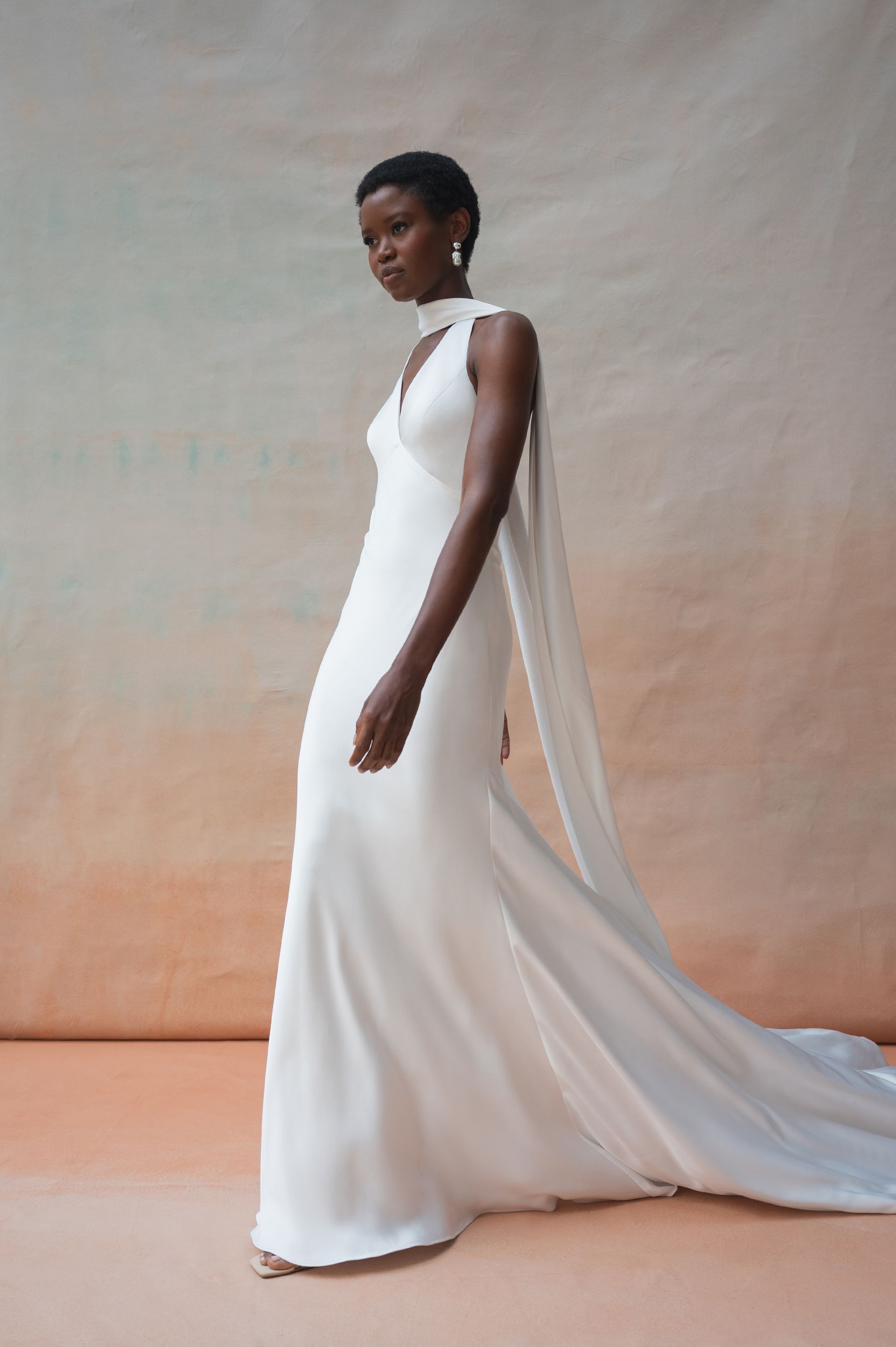 A person wears a minimalist white floor-length gown with a high-neck collar