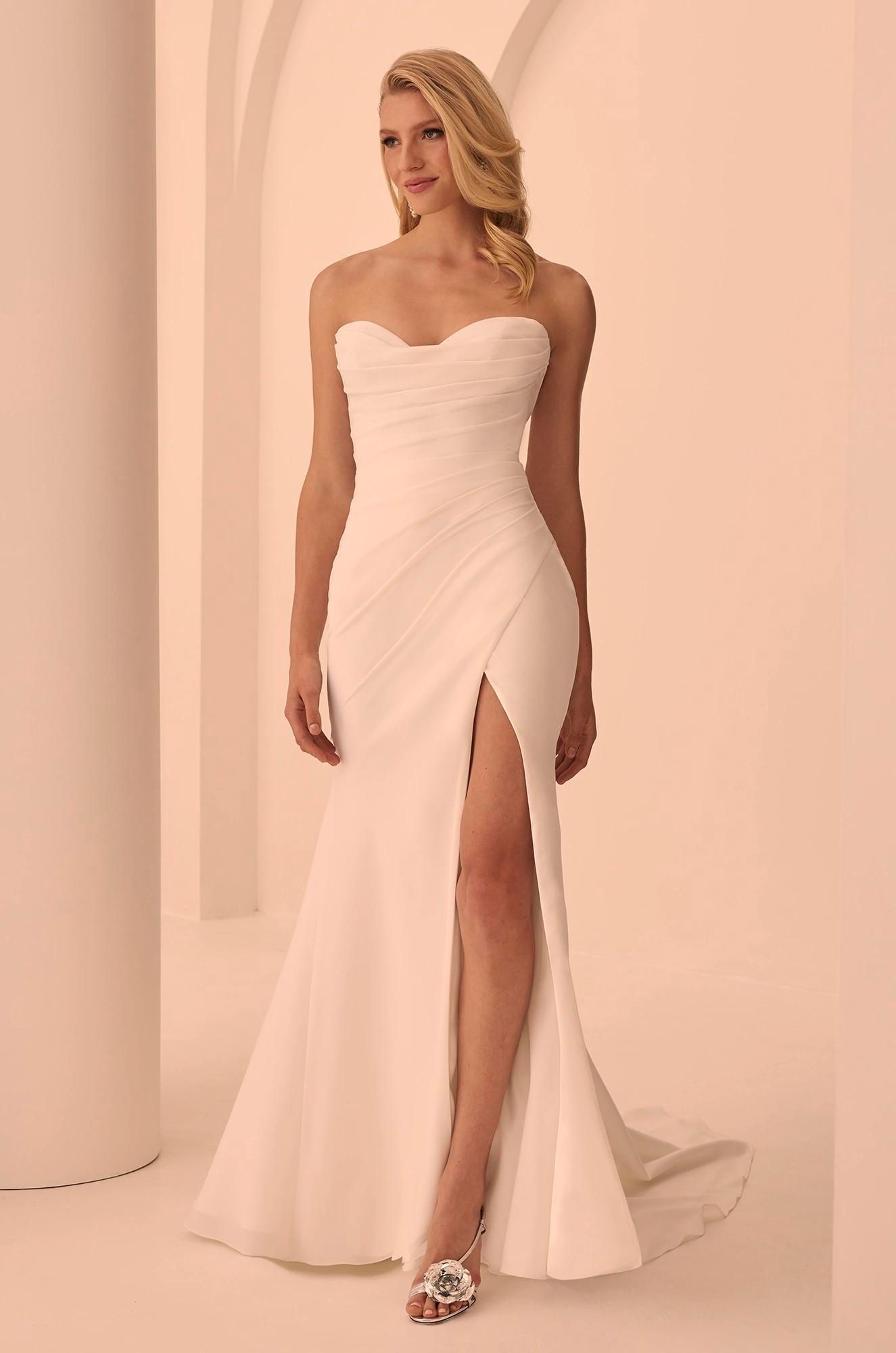 A woman models a floor-length, strapless cream-colored gown with a sweetheart neckline and a high thigh slit.