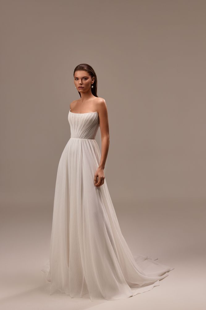 A person models a strapless, white A-line wedding gown with a pleated, fitted bodice and a flowing tulle skirt.