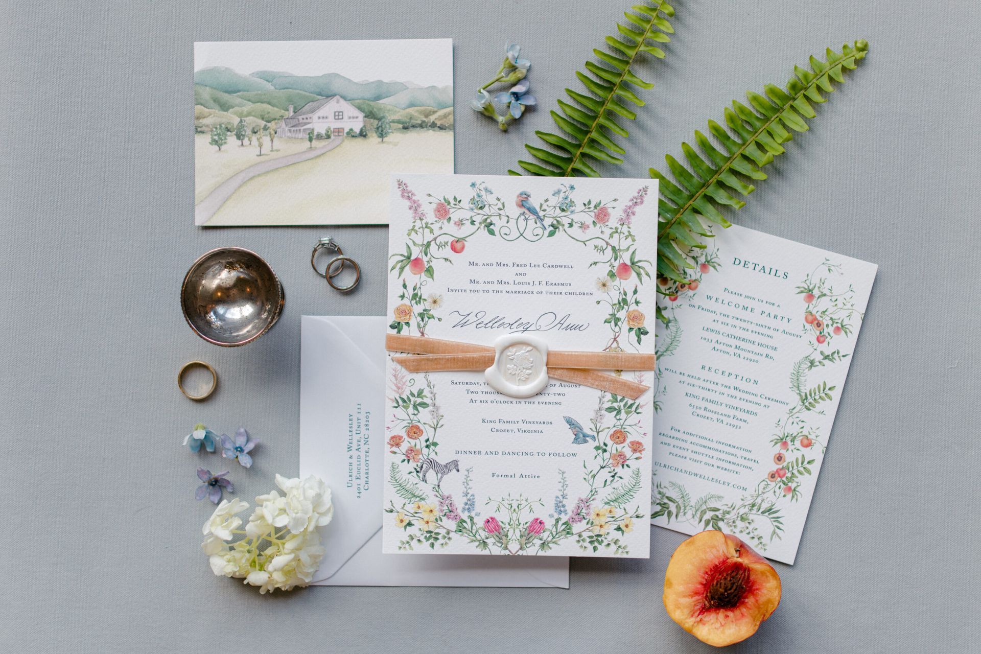 A wedding invitation flat lay with floral stationery, a venue illustration, a peach, greenery,