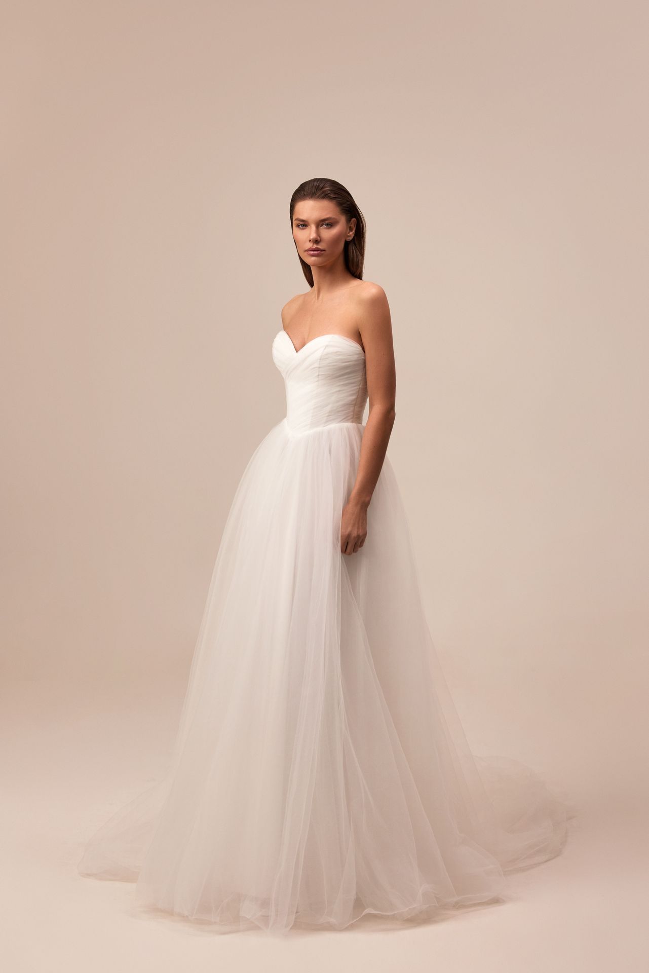 A model wears a strapless, white, A-line wedding gown with a sweetheart bodice and a flowing, layered tulle skirt.