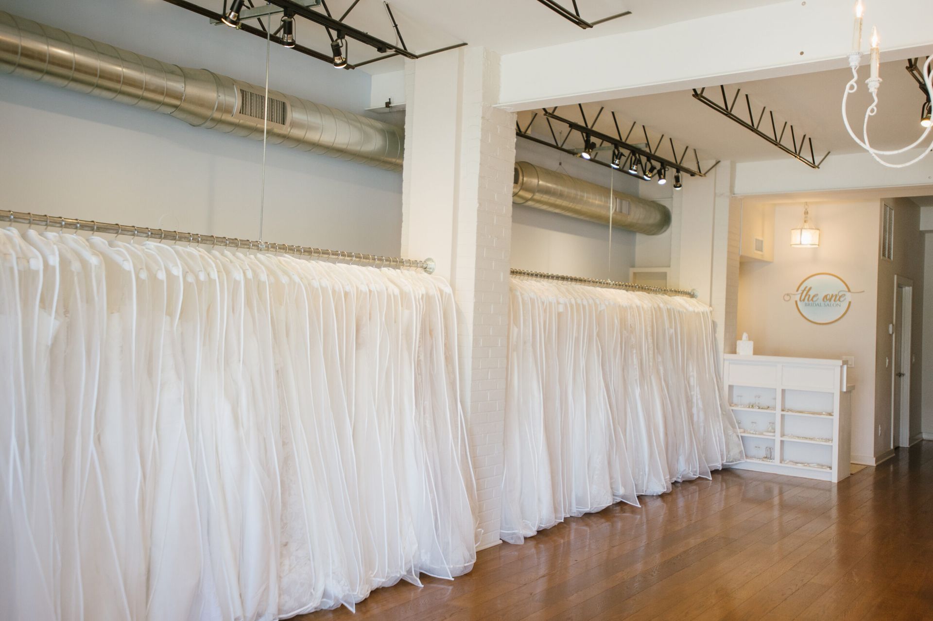 Rows of white wedding dresses hanging on racks in a bright boutique with a wooden floor.
