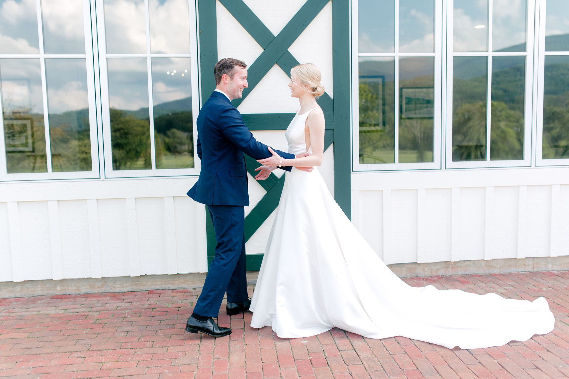 A bride and groom standing on a brick patio in front of a white building, looking at each other during a first look.