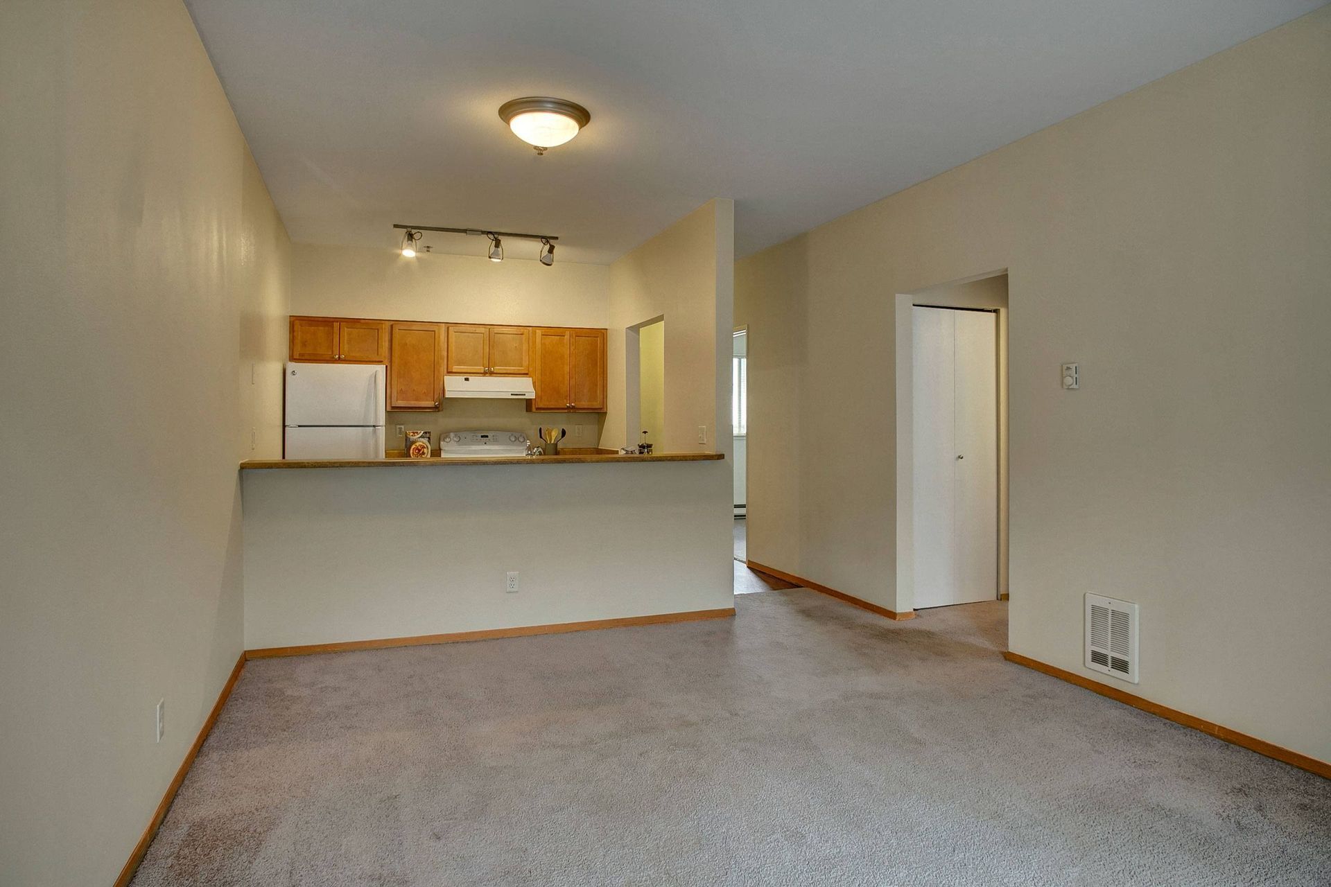 An empty living room with a kitchen in the background.