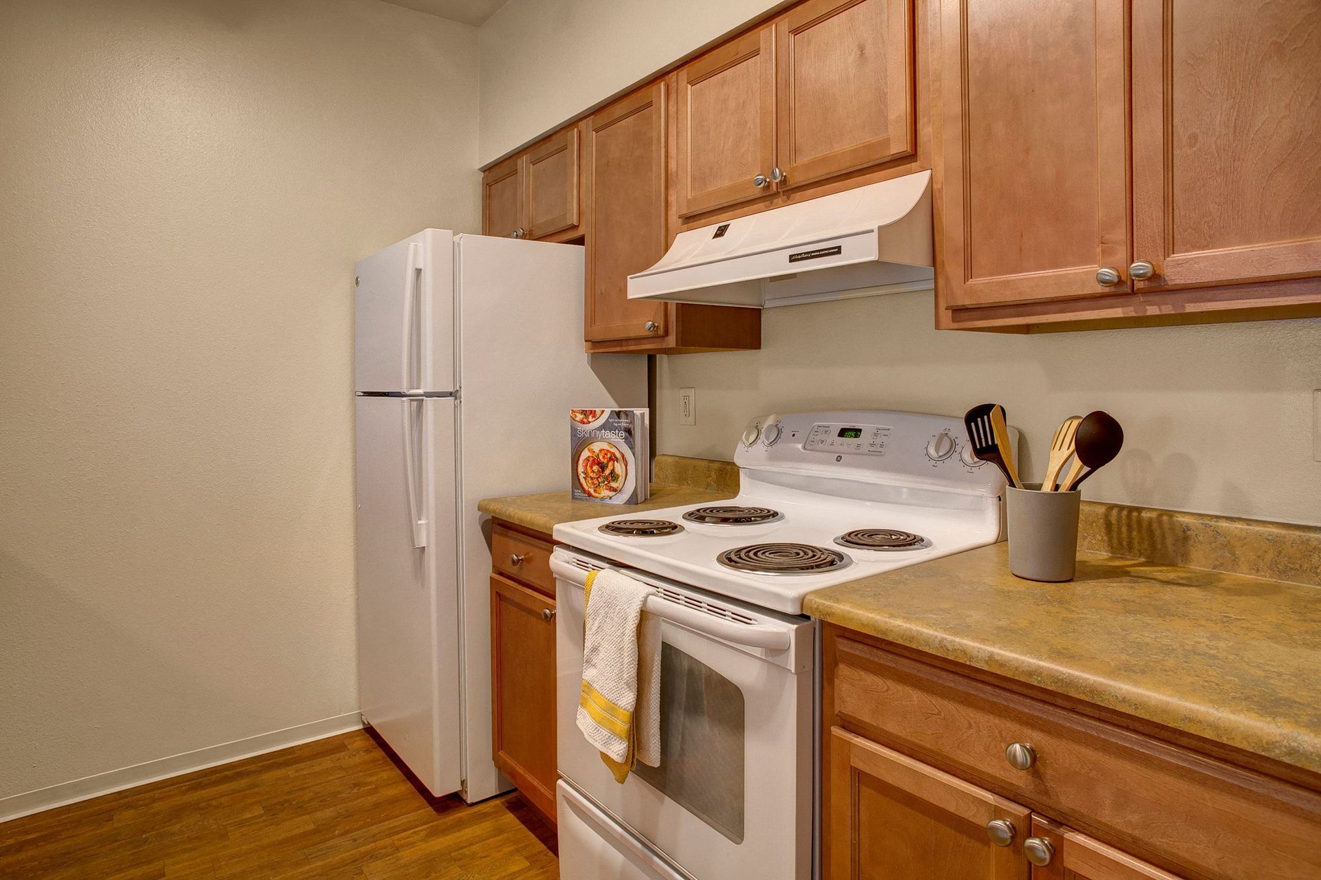 A kitchen with a stove, refrigerator, and wooden cabinets.