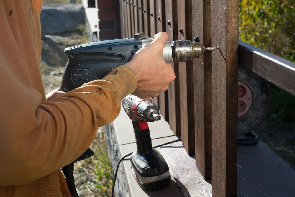 a man is using a drill on a wooden fence