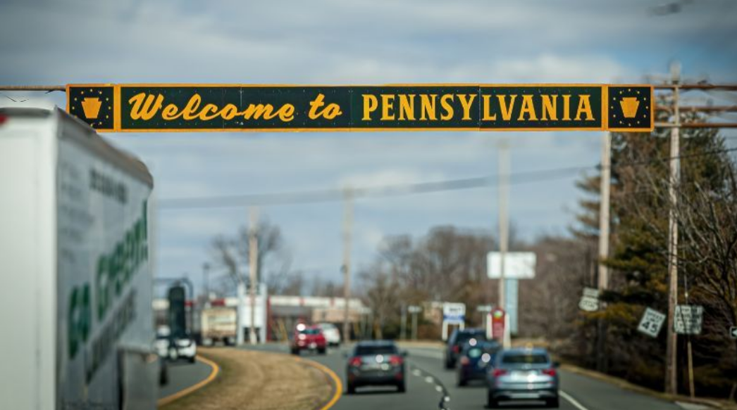 A welcome to pennsylvania sign is hanging over a highway.