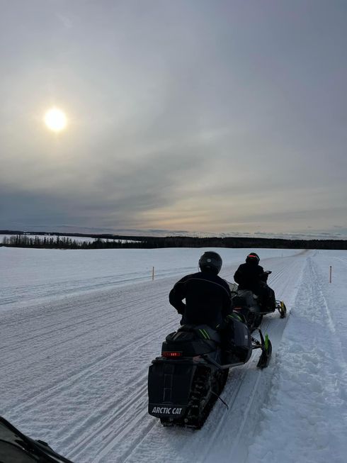 a group of people are riding snowmobiles down a snowy road .