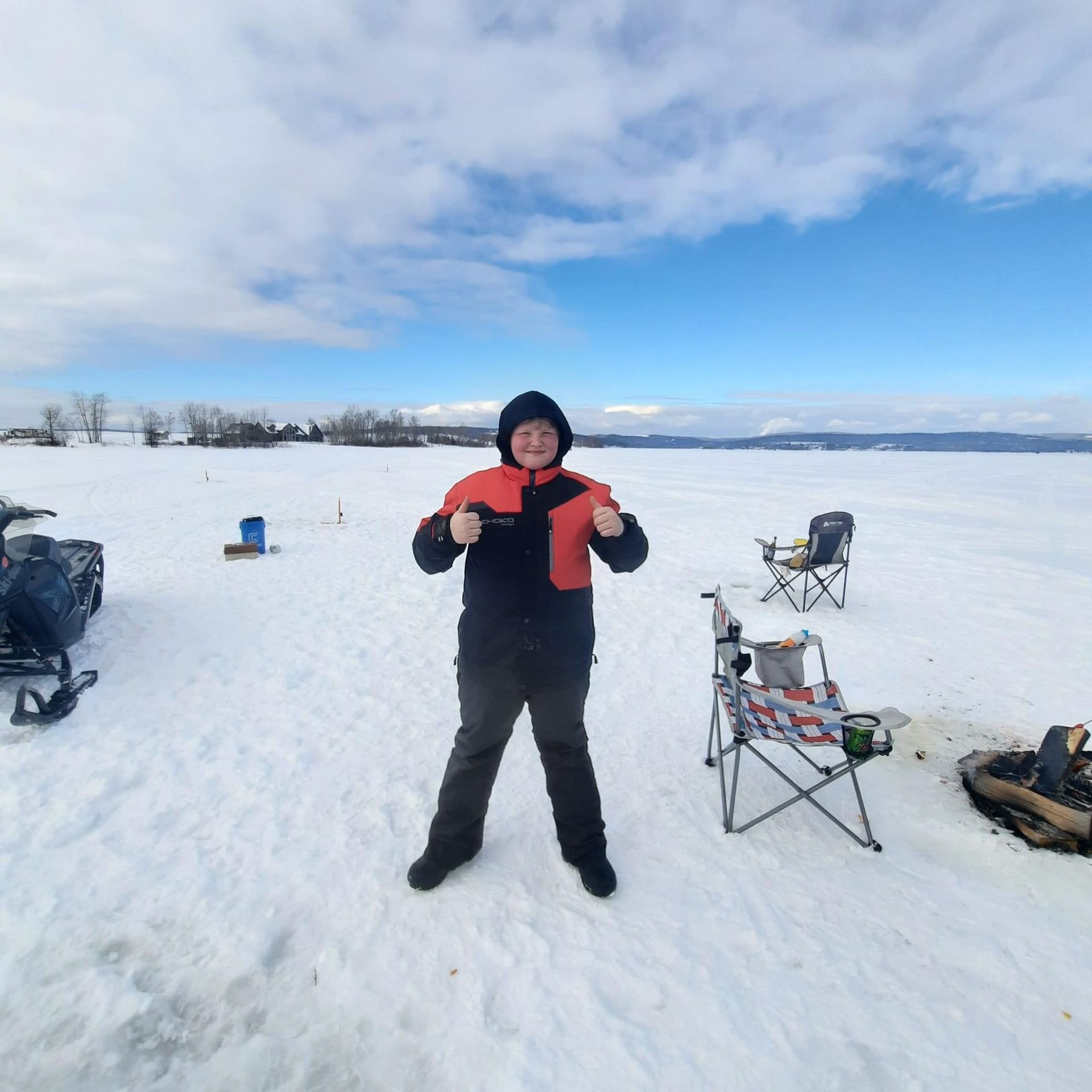 a person standing in the snow with a snowmobile in the background