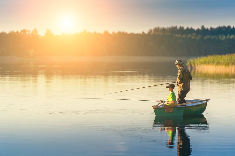 a man and a boy are fishing in a boat on a lake at sunset .