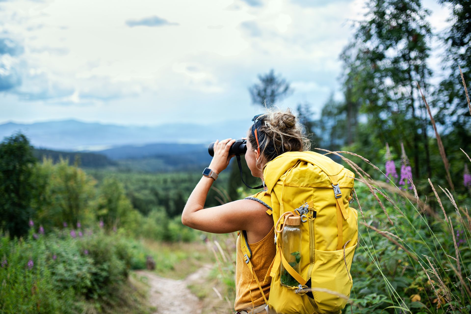 a woman with a yellow backpack is looking through binoculars .