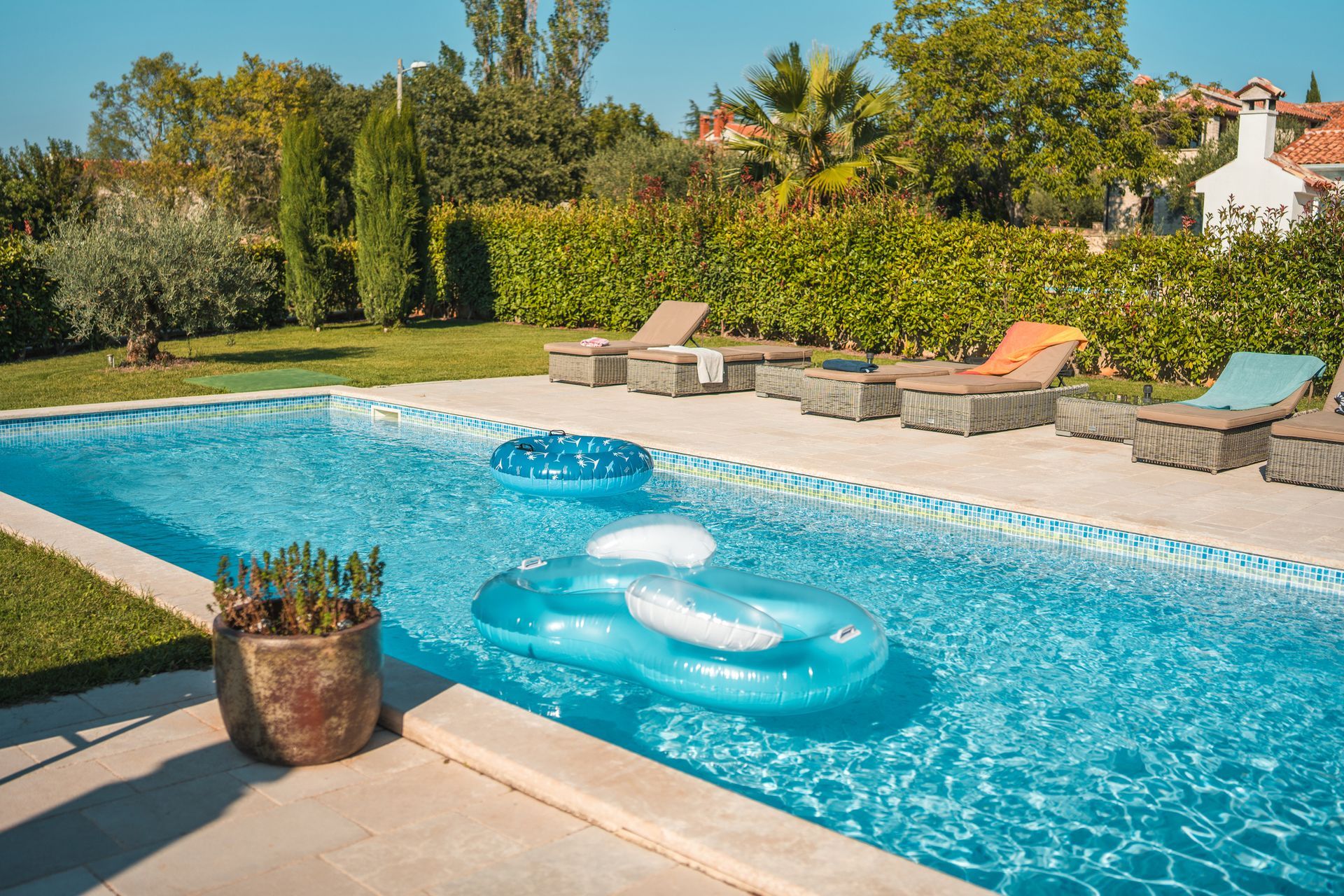 Swimming pool with two inflatable floats and lounge chairs on a sunny day.