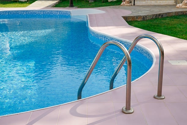 Swimming pool with blue water, tile surround, and metal ladder.