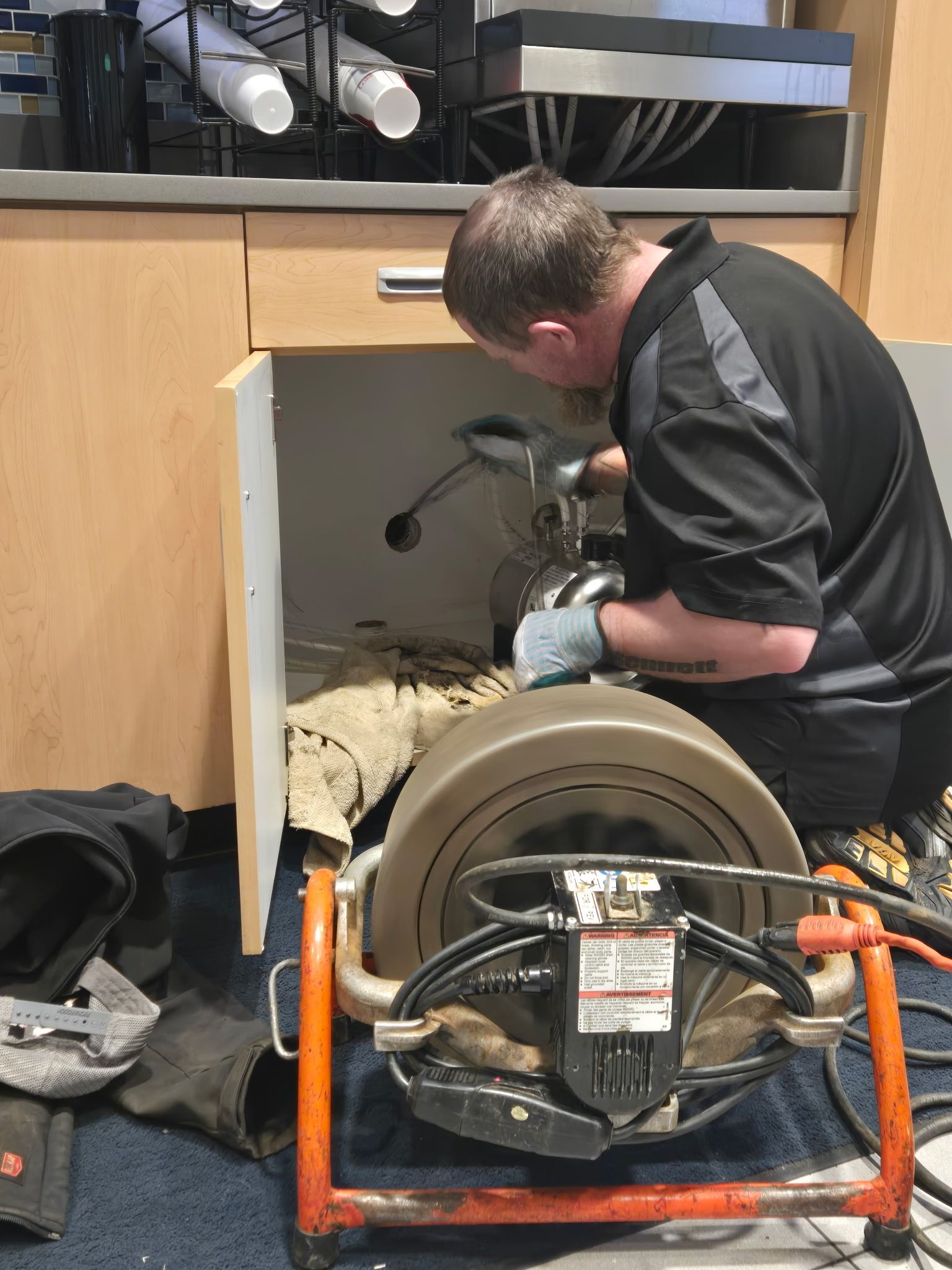 A man is working on a drain under a sink with a machine.
