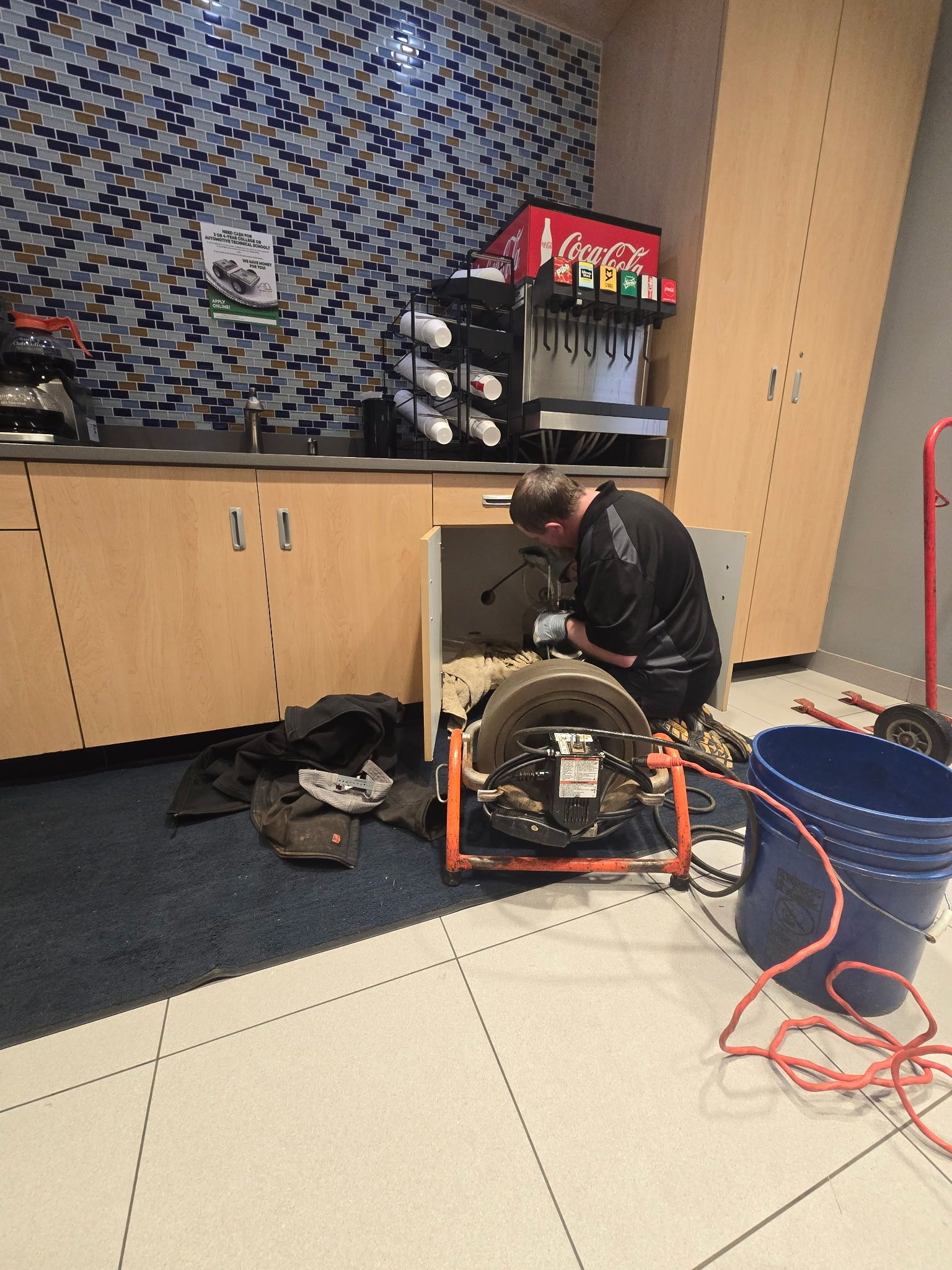 A man is working on a drain in a kitchen.
