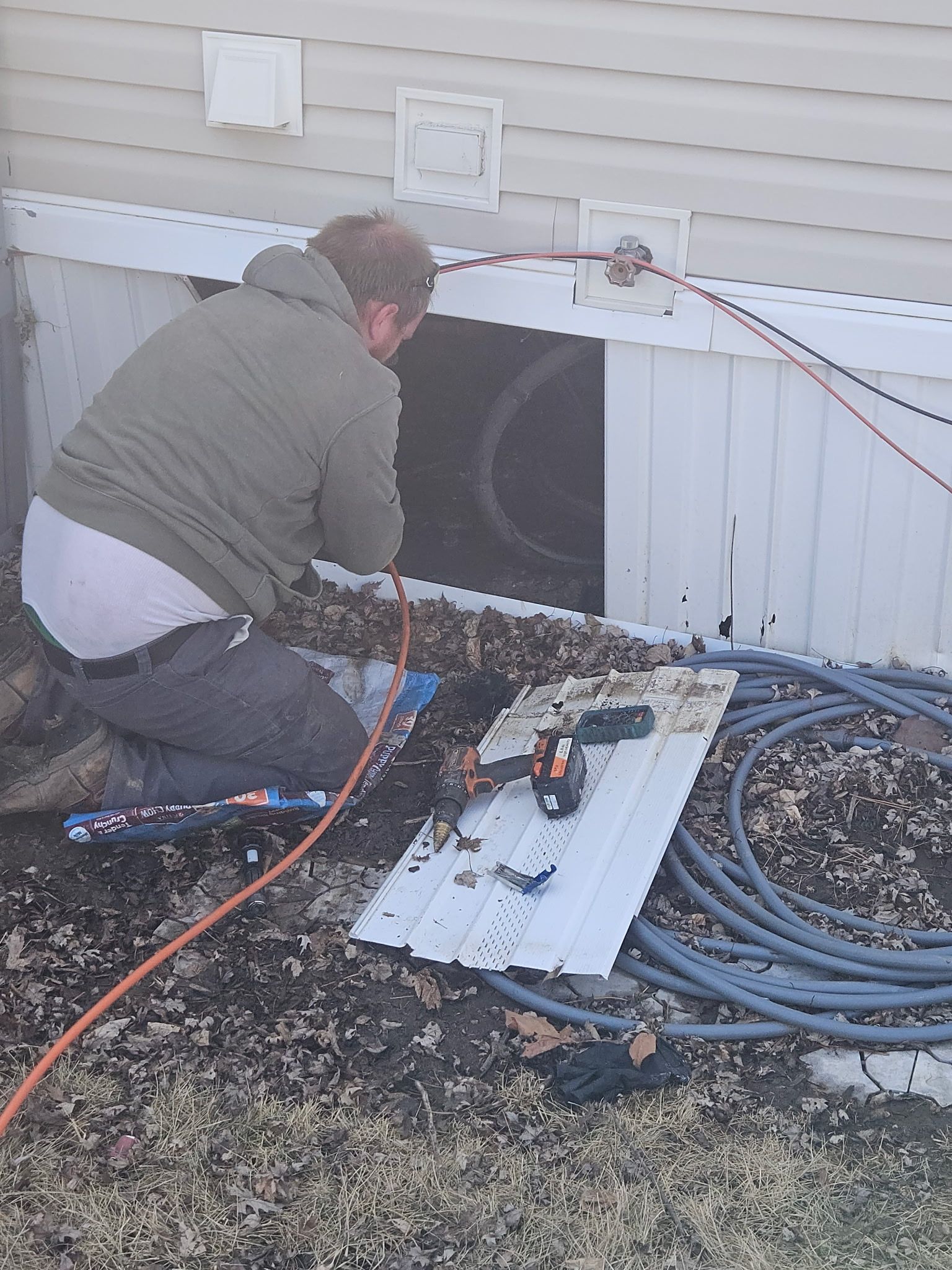 A man is kneeling down in front of a house working on a window.