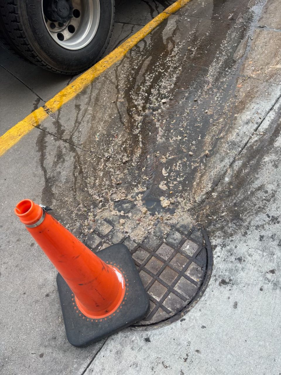 An orange traffic cone is sitting next to a manhole cover