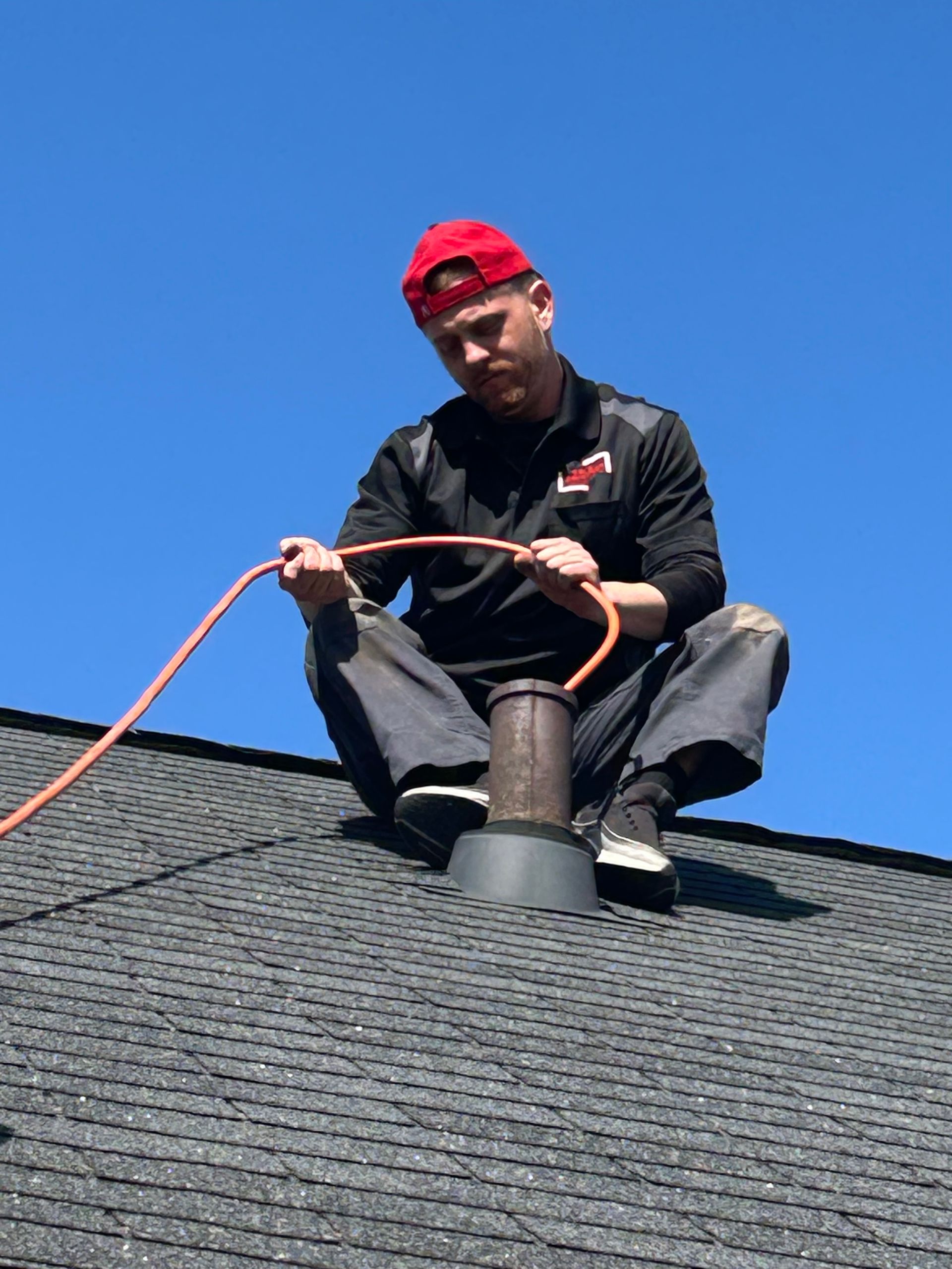 A man is sitting on top of a roof holding a hose