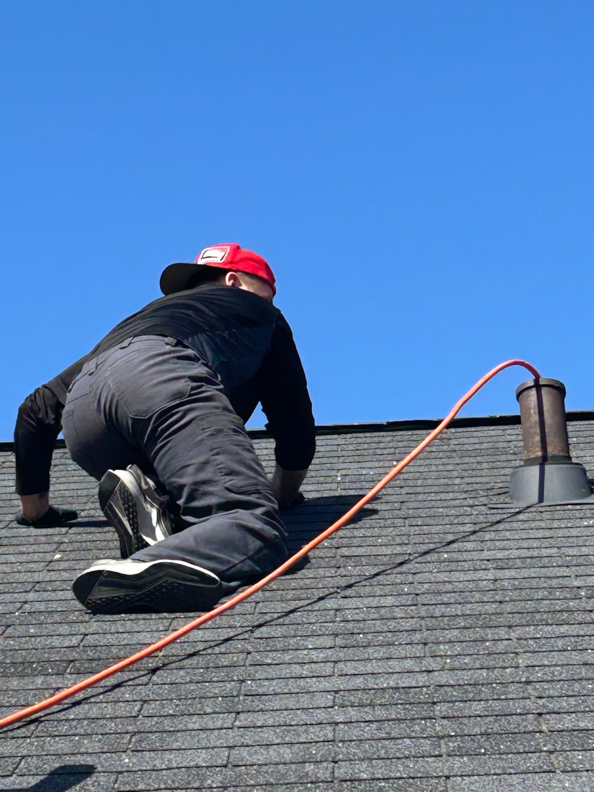 A man is kneeling on a roof with a hose attached to him