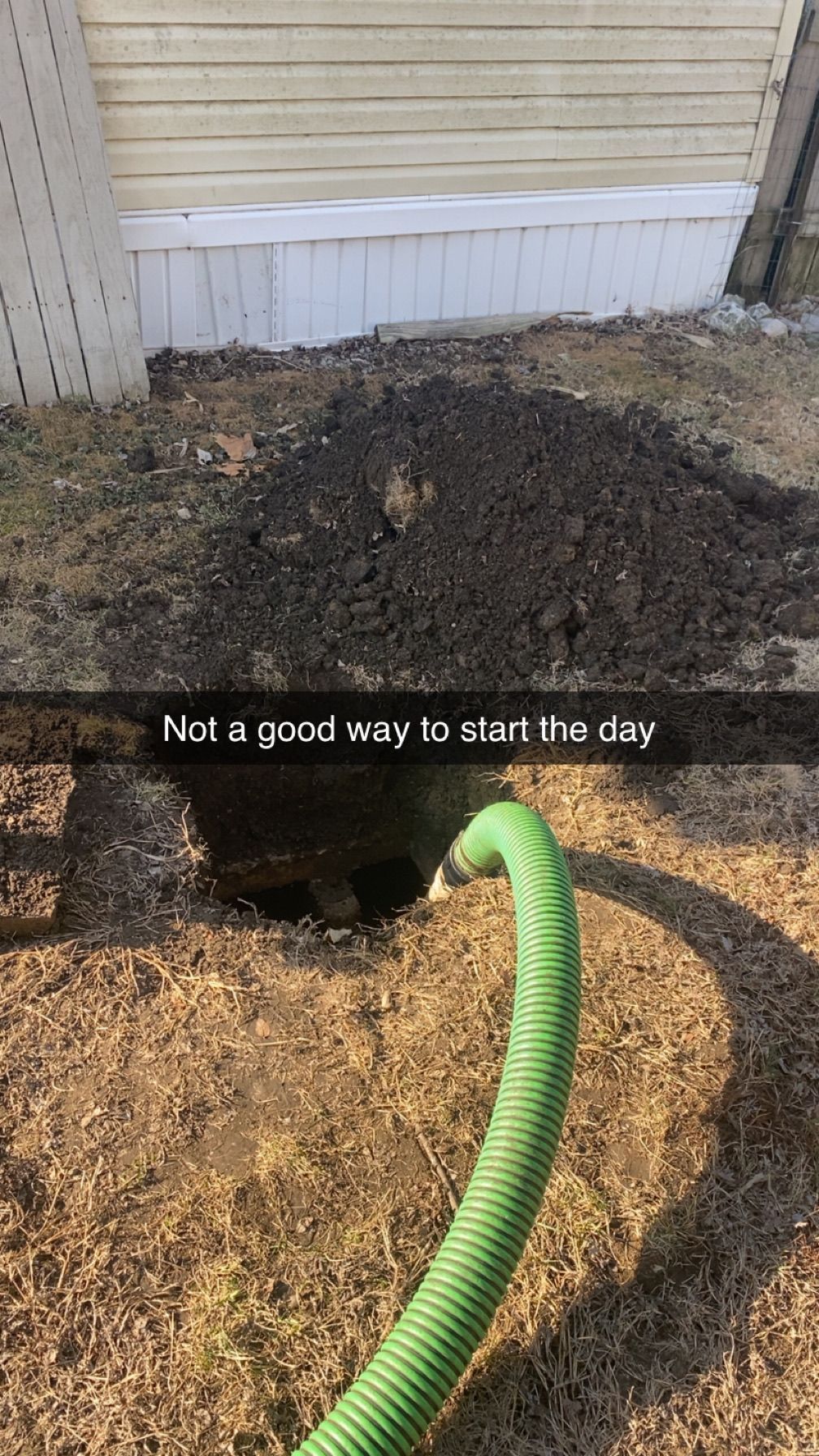 A green hose is connected to a hole in the ground.