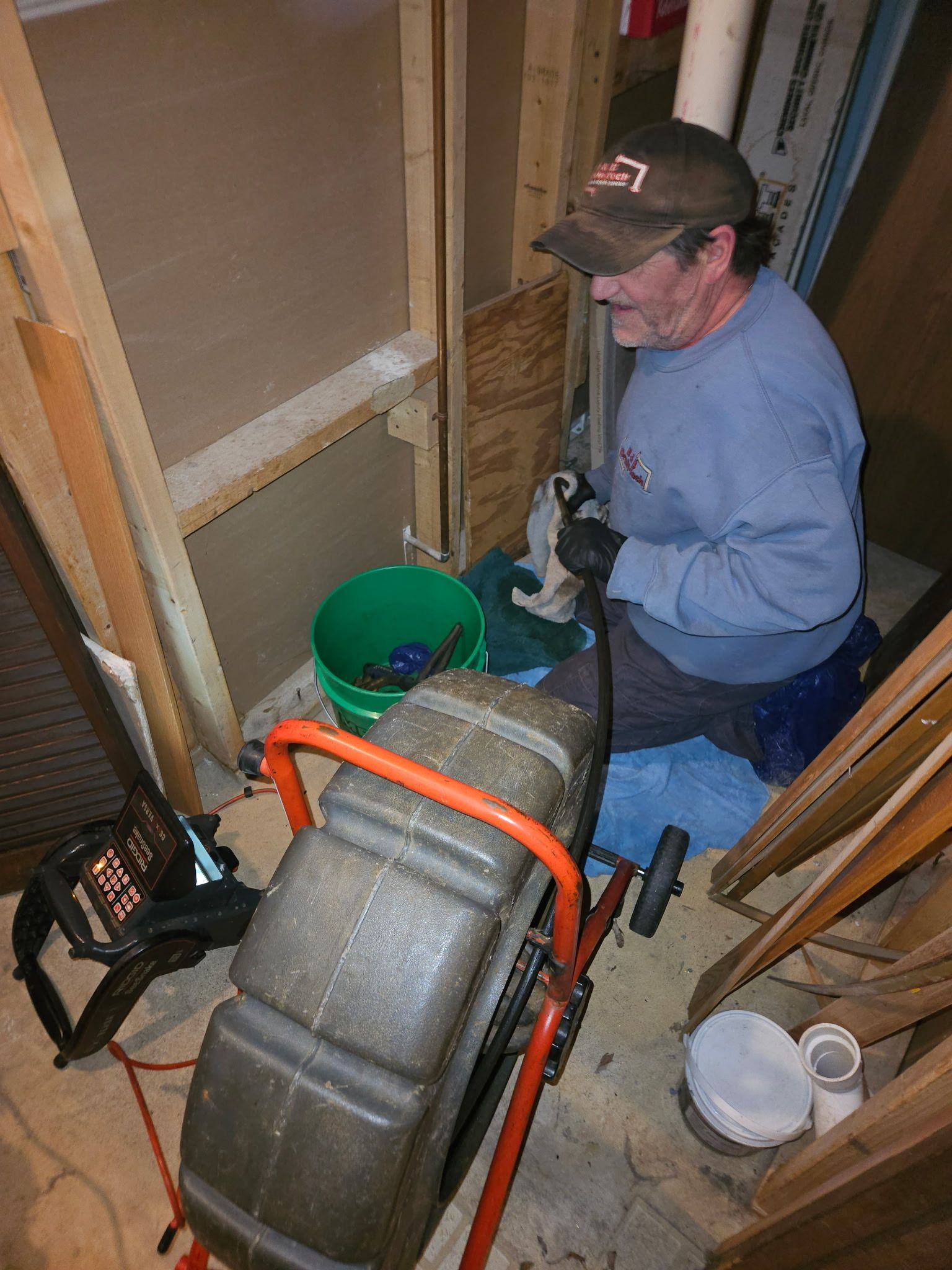 A man is kneeling down in a room using a drain cleaner.