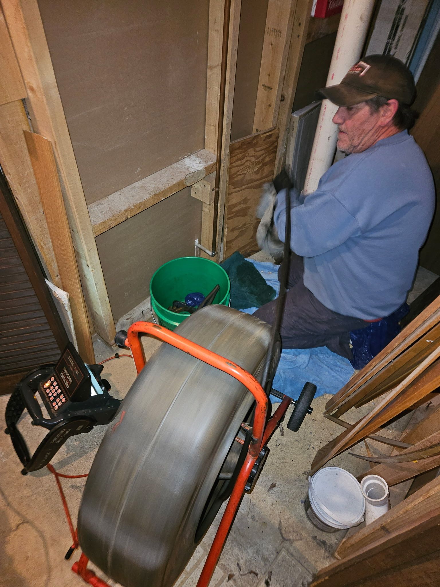 A man is sitting on the floor using a drain cleaner.