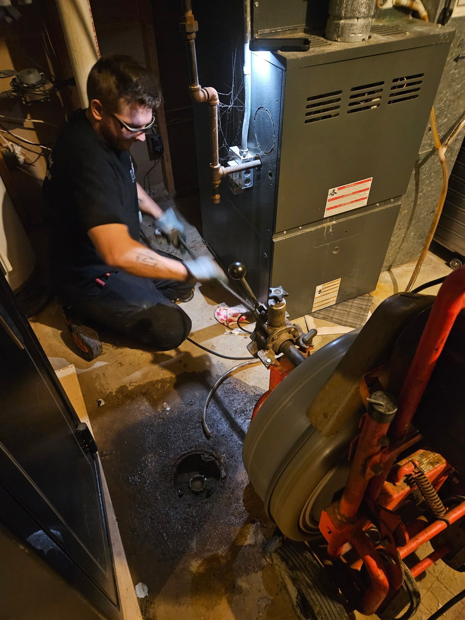 A man is kneeling down in front of an air conditioner in a basement.