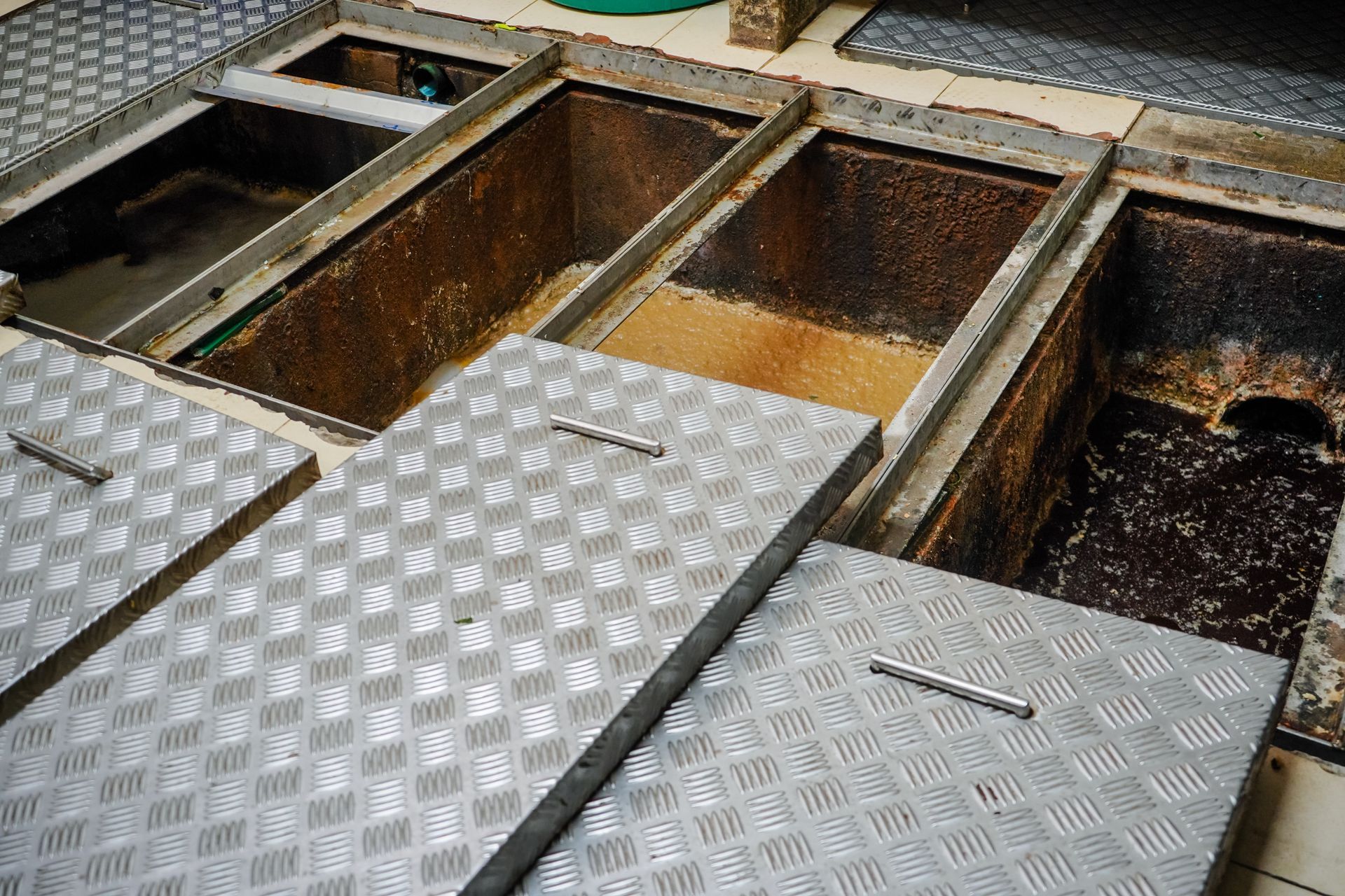 Open metal floor hatches revealing underground utility pits with water and gravel.