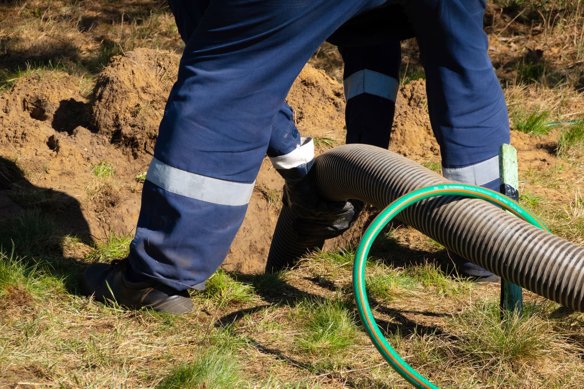 Workers handling a large corrugated hose on a grassy dirt slope