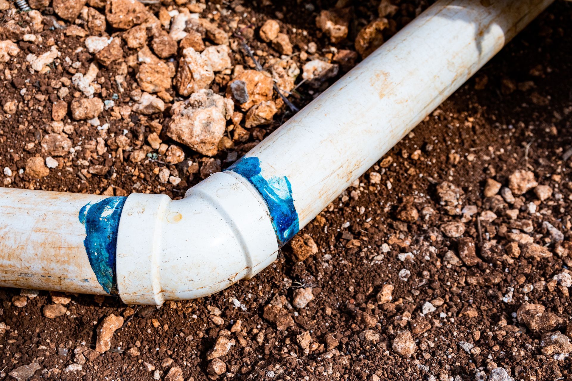 White PVC pipe joint with blue sealant leaking into brown soil soil
