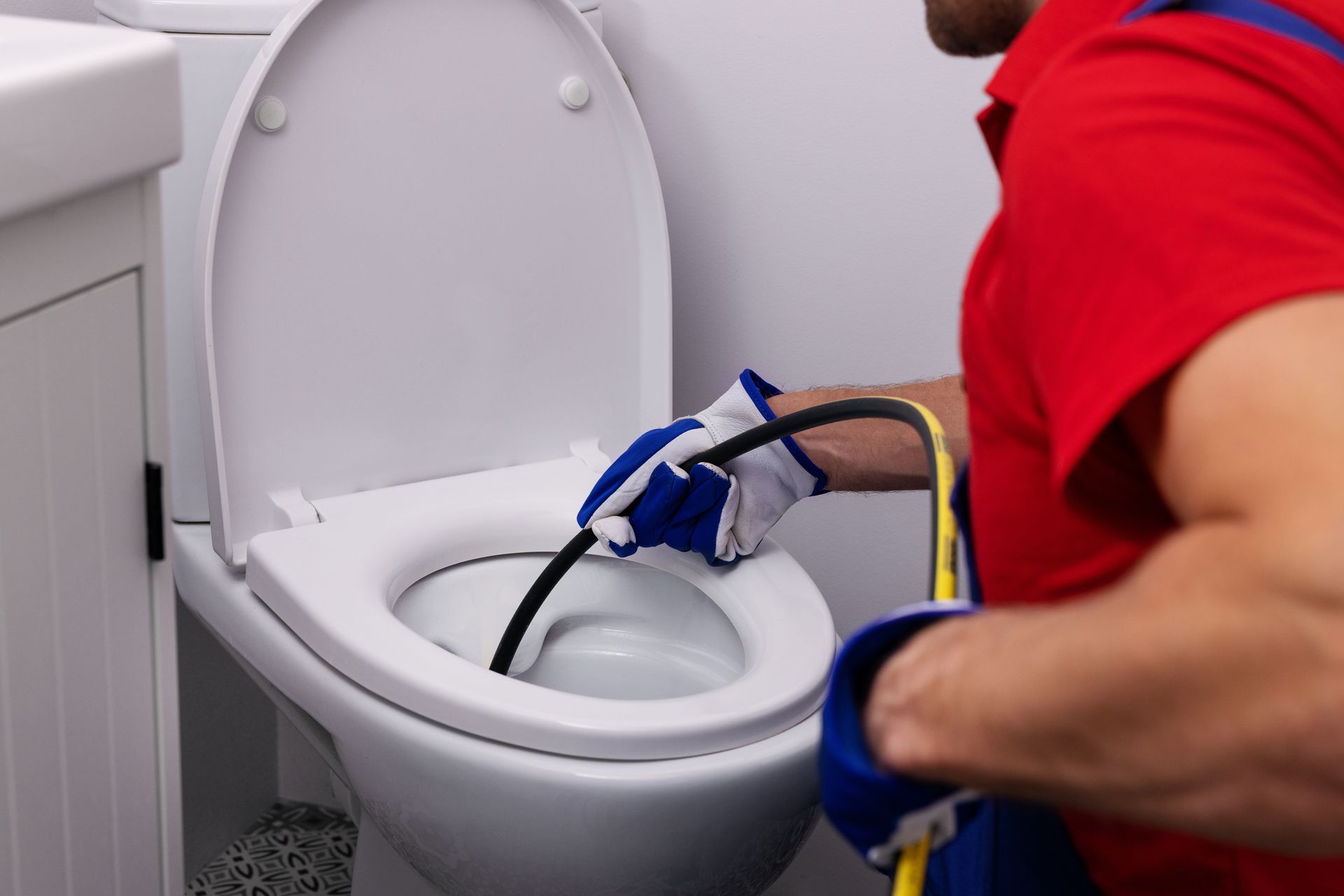 Plumber unclogging a white toilet with a drain snake in a bathroom