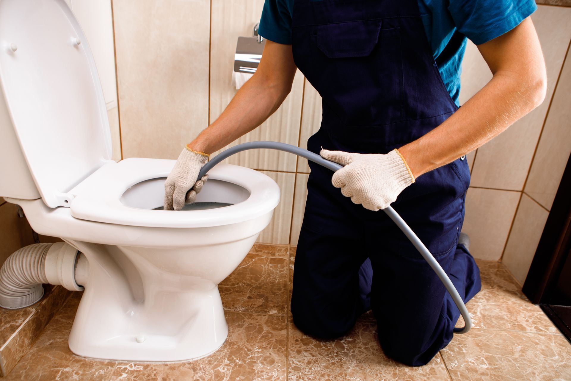Plumber using a drain snake to unclog a toilet in a bathroom