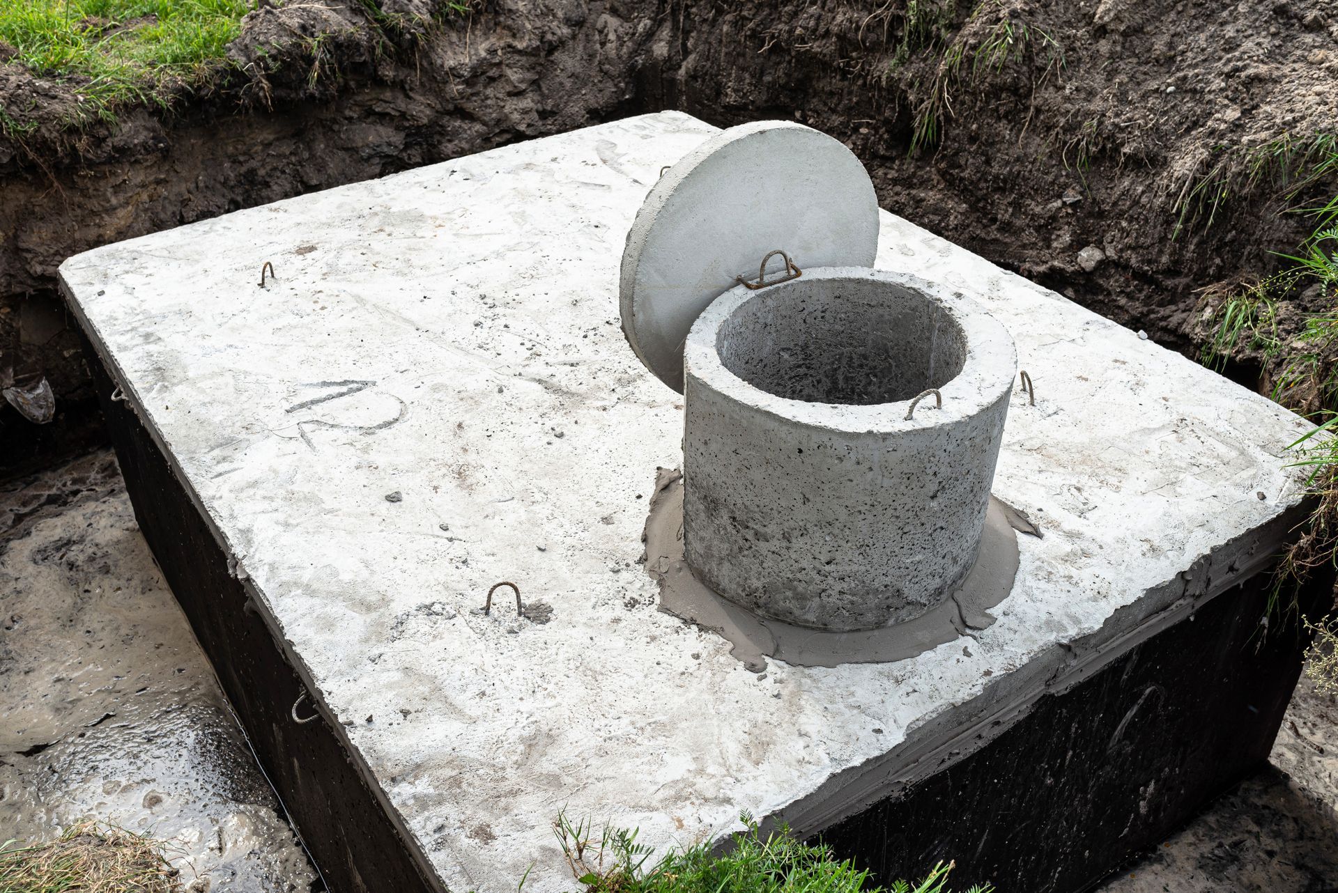 Concrete manhole cover with a round opening on a square slab outdoors in dirt and grass