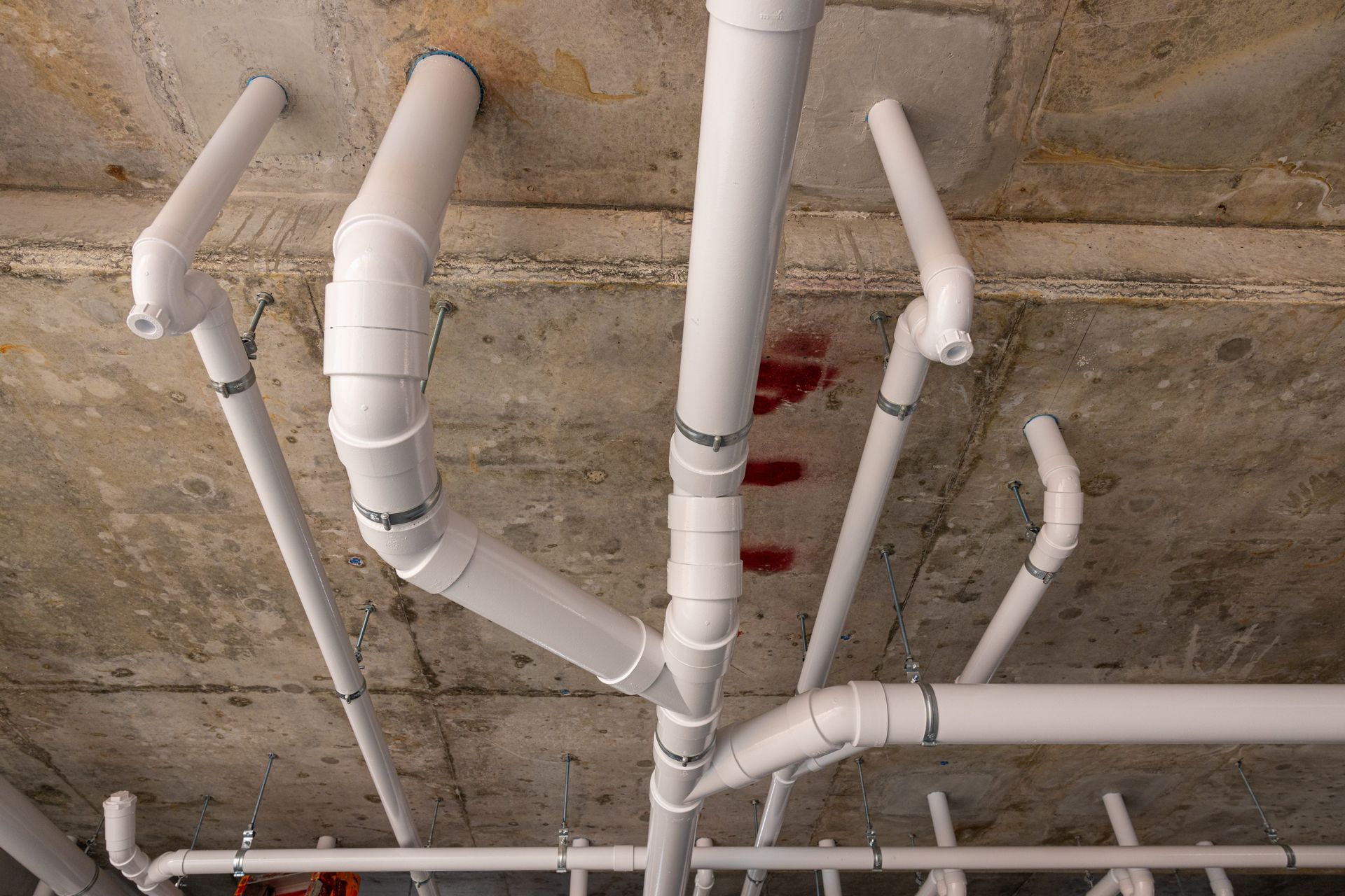 White PVC pipes and fittings running across a rough concrete ceiling