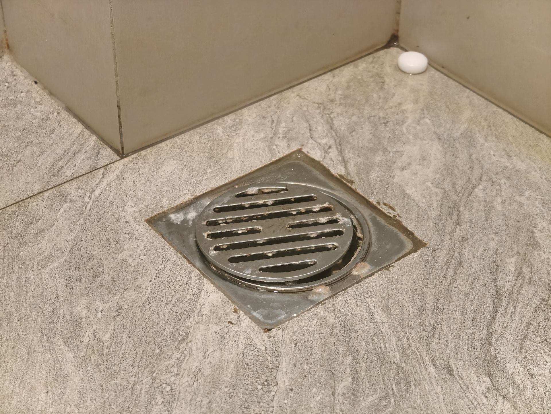 Floor drain grate in a beige tiled bathroom corner