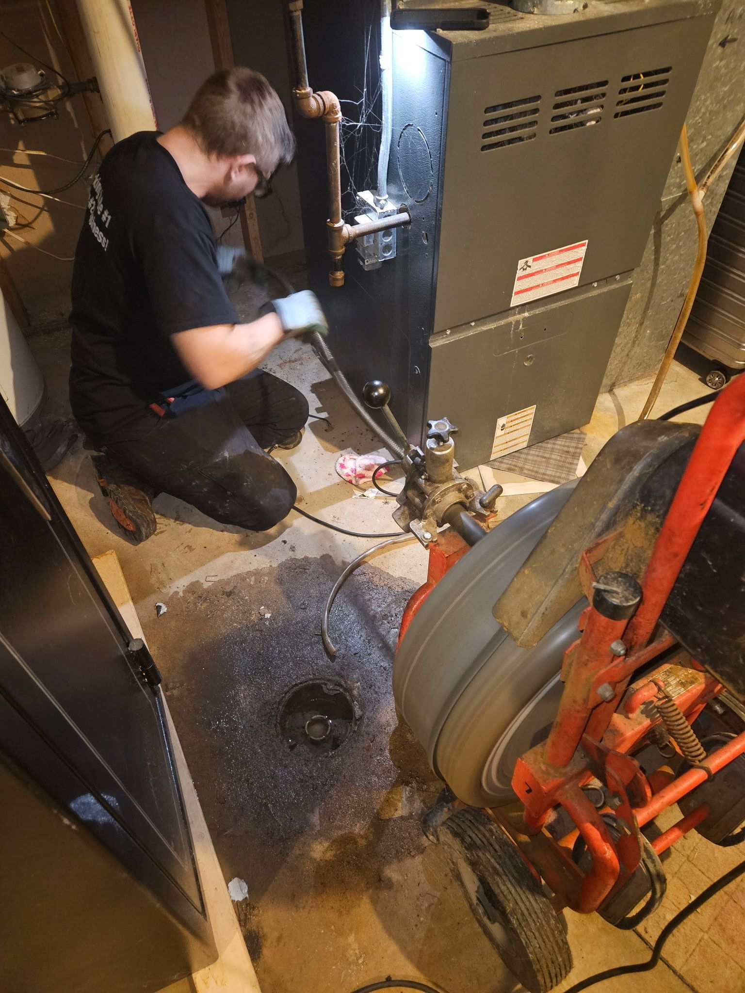 A man is kneeling down in front of a furnace in a basement.