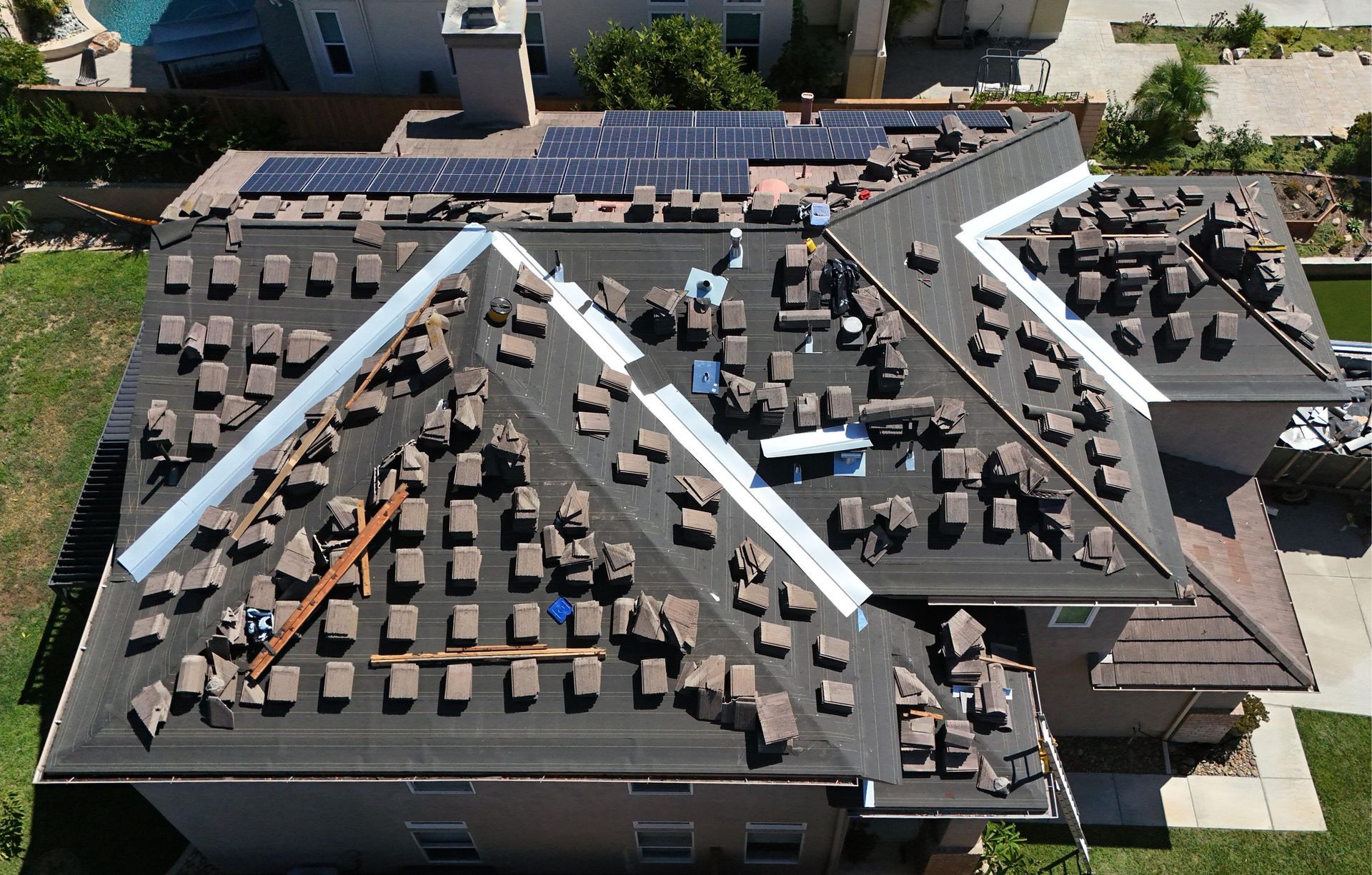 Roof partially stripped of tiles, revealing underlayment; solar panels, house, daytime.