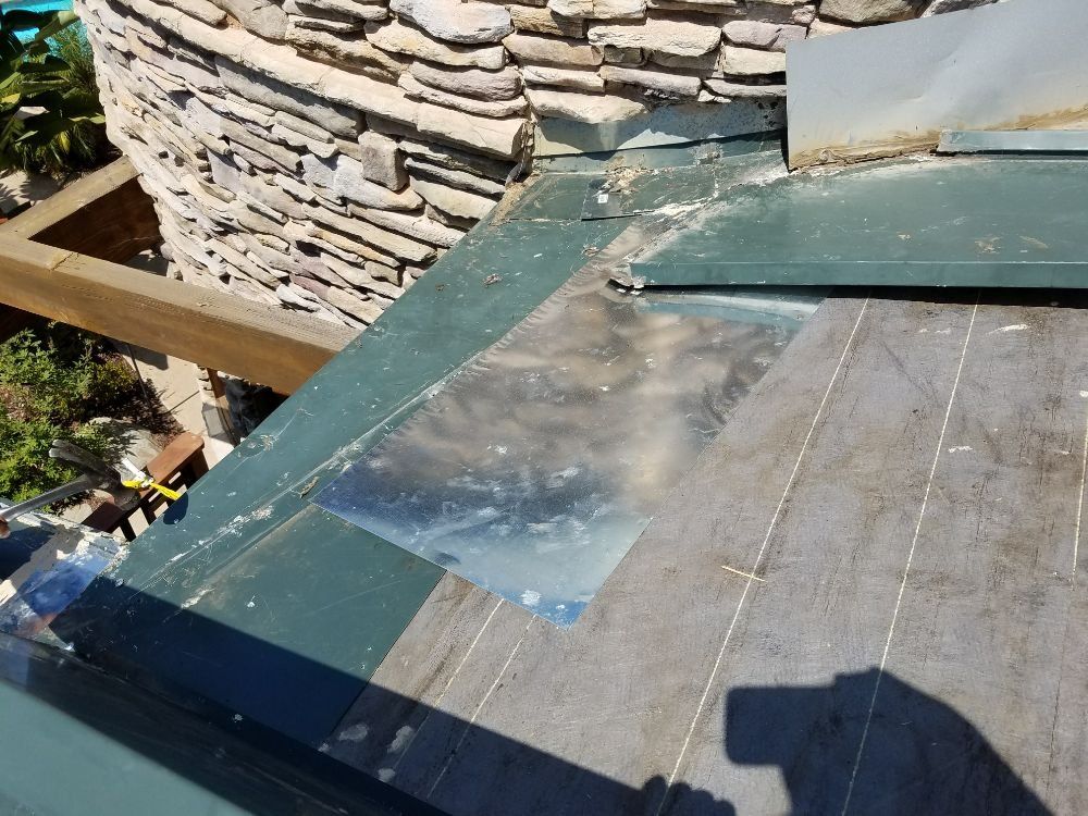 A close up of a roof with a stone wall in the background.