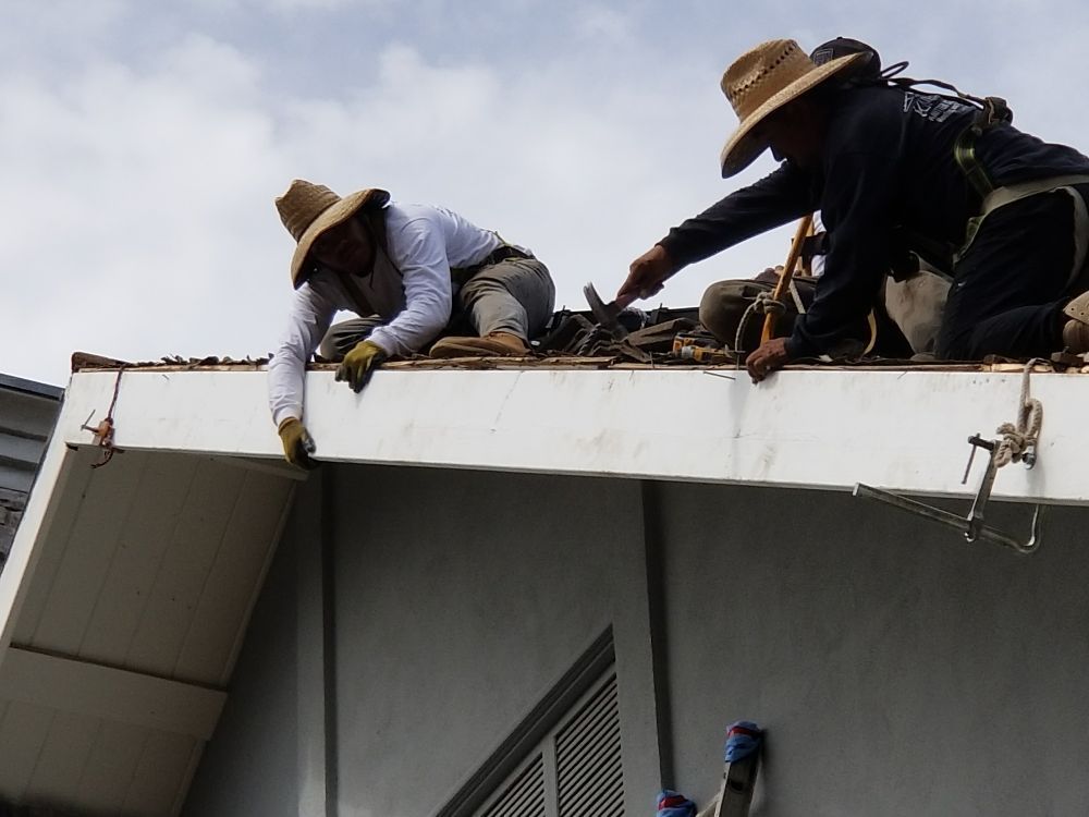 Two men wearing hats are working on the roof of a building
