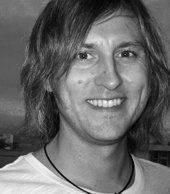 A man with long hair is smiling in a black and white photo.