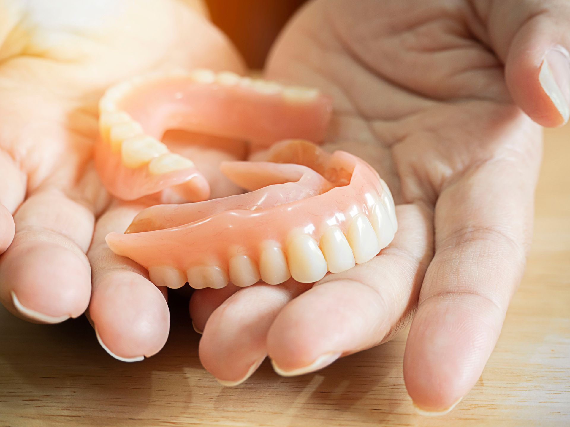 Hands holding upper and lower full dentures at Dentures In A Day PLC in Wyoming, MI
