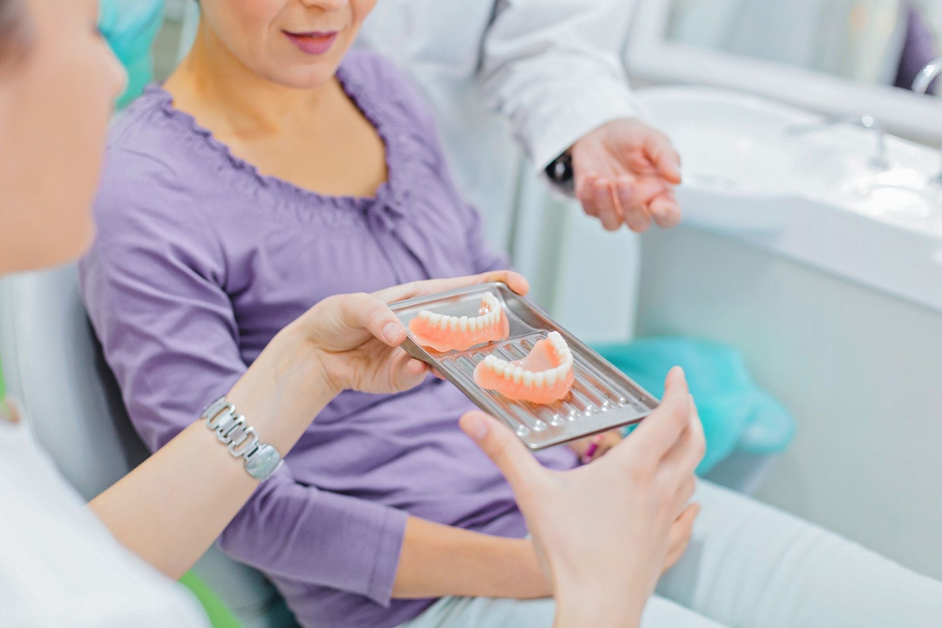 Dentist showing dentures to female patient during local denture care consultation at dental clinic.