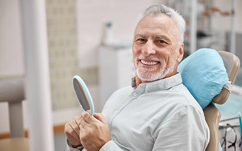 Happy Senior Man Holding a Mirror — Grand Rapids, MI — Dentures In a Day